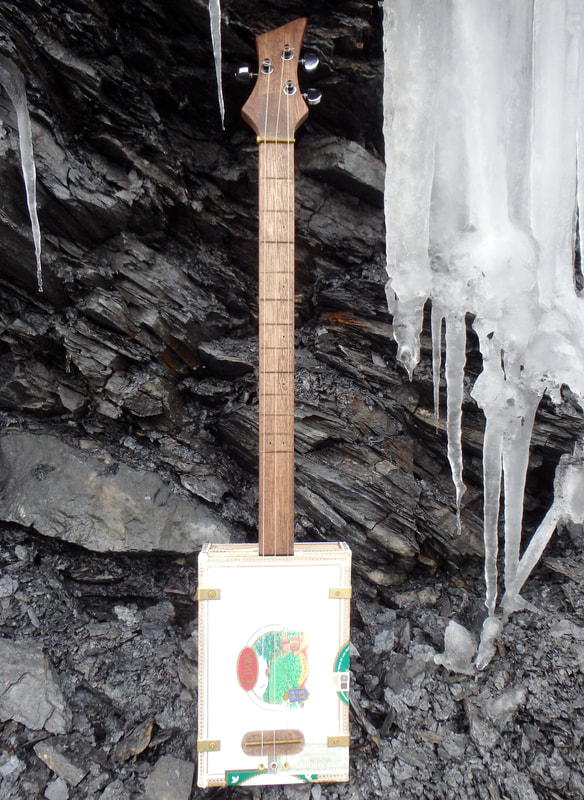 White Cuaba cigar box guitar from Wires and Wood in front of an ice wall.