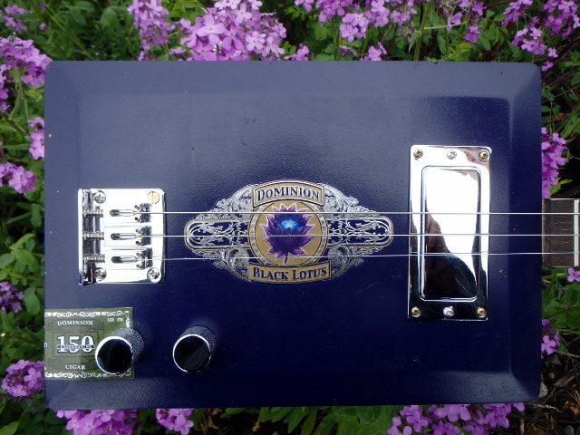 Dominion Black Lotus purple cigar box from Wires and Wood in front of purple flowers.