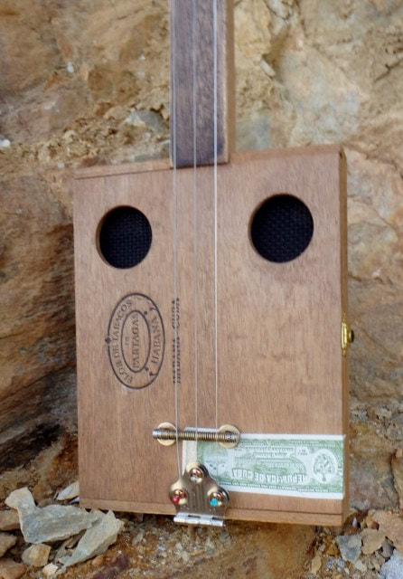Flor De Tabaco wood front of a cigar box guitar from Wires and Wood up against a rock wall.