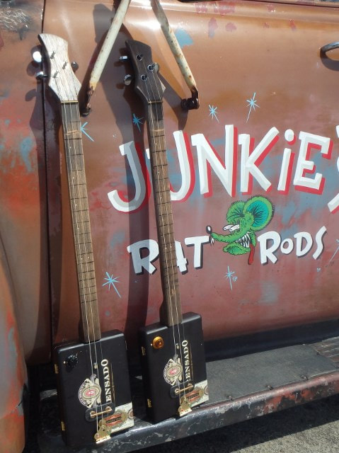 Two black Wires and Wood Cigar Box Guitars in front of an old truck